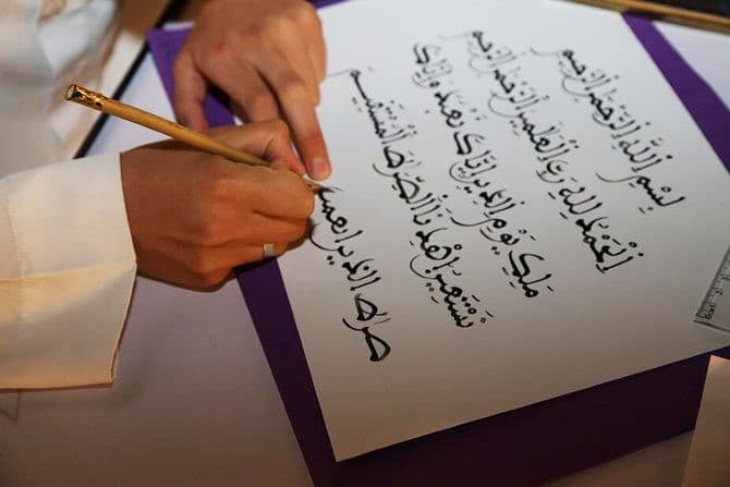 A calligrapher writing Arabic script with a traditional reed pen